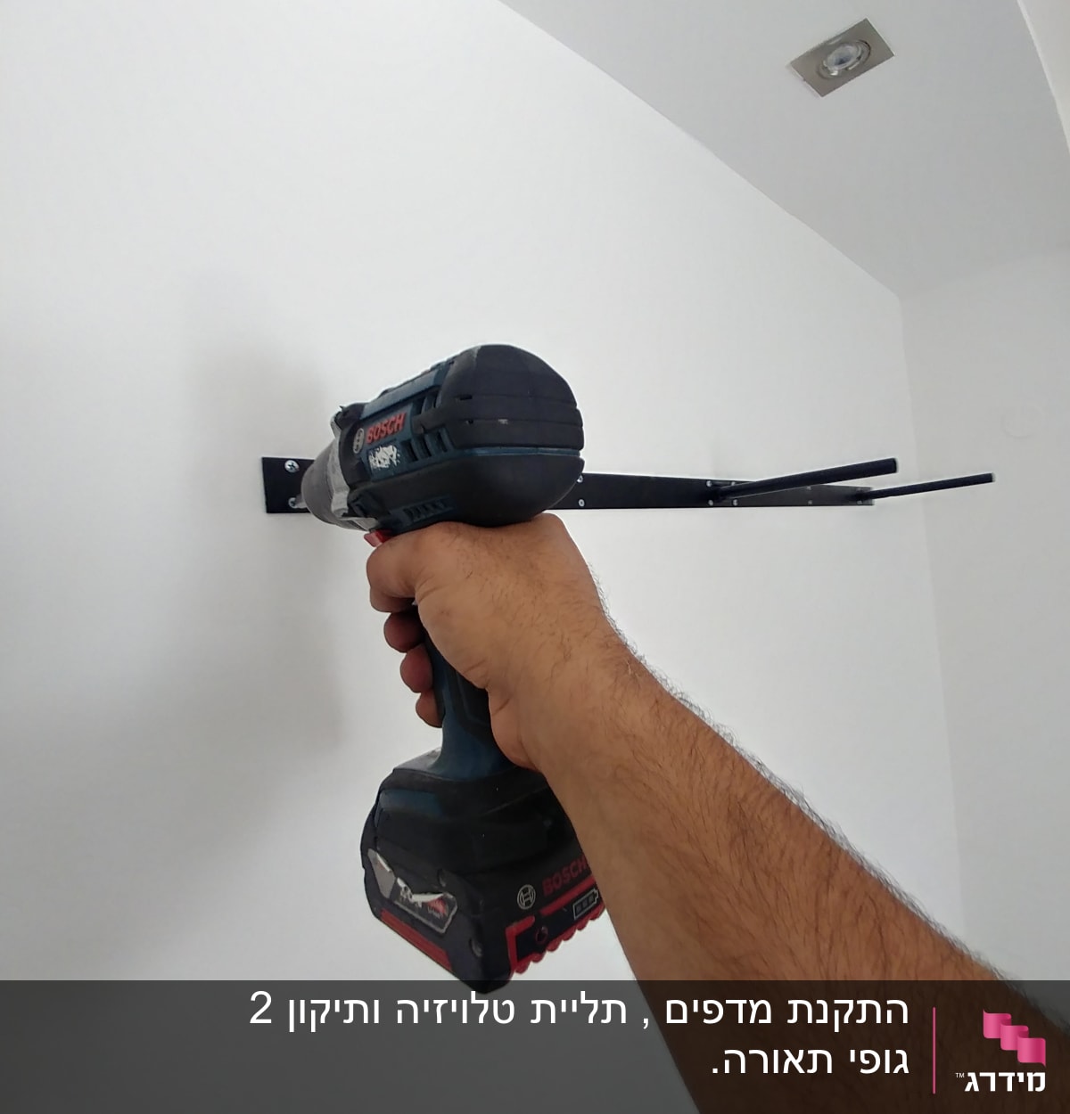 יד מחזיקה מברגה חשמלית על קיר לבן